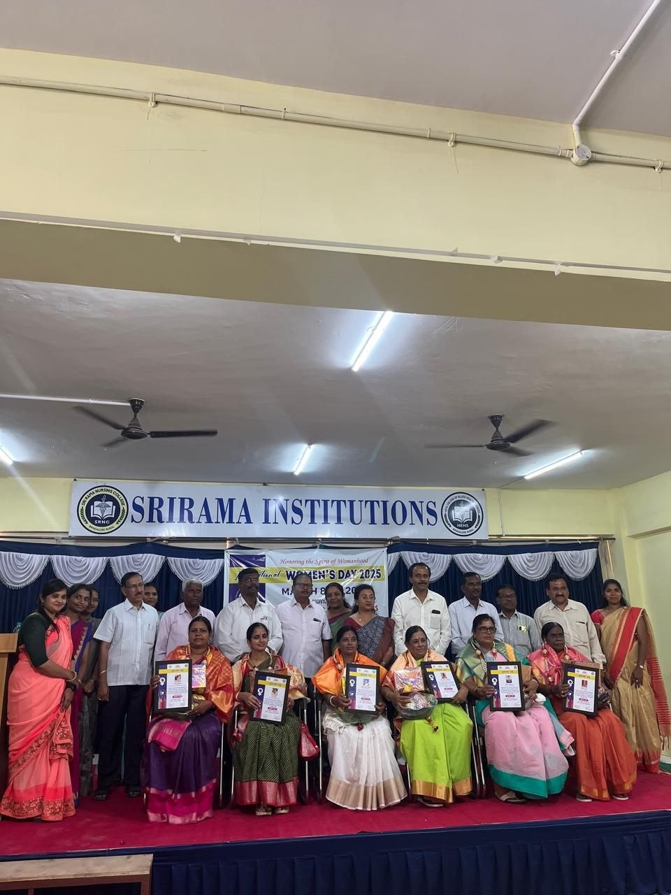 Group photograph of women being honoured with certificates on stage beneath a Srirama Institutions banner at the Women's Day programme