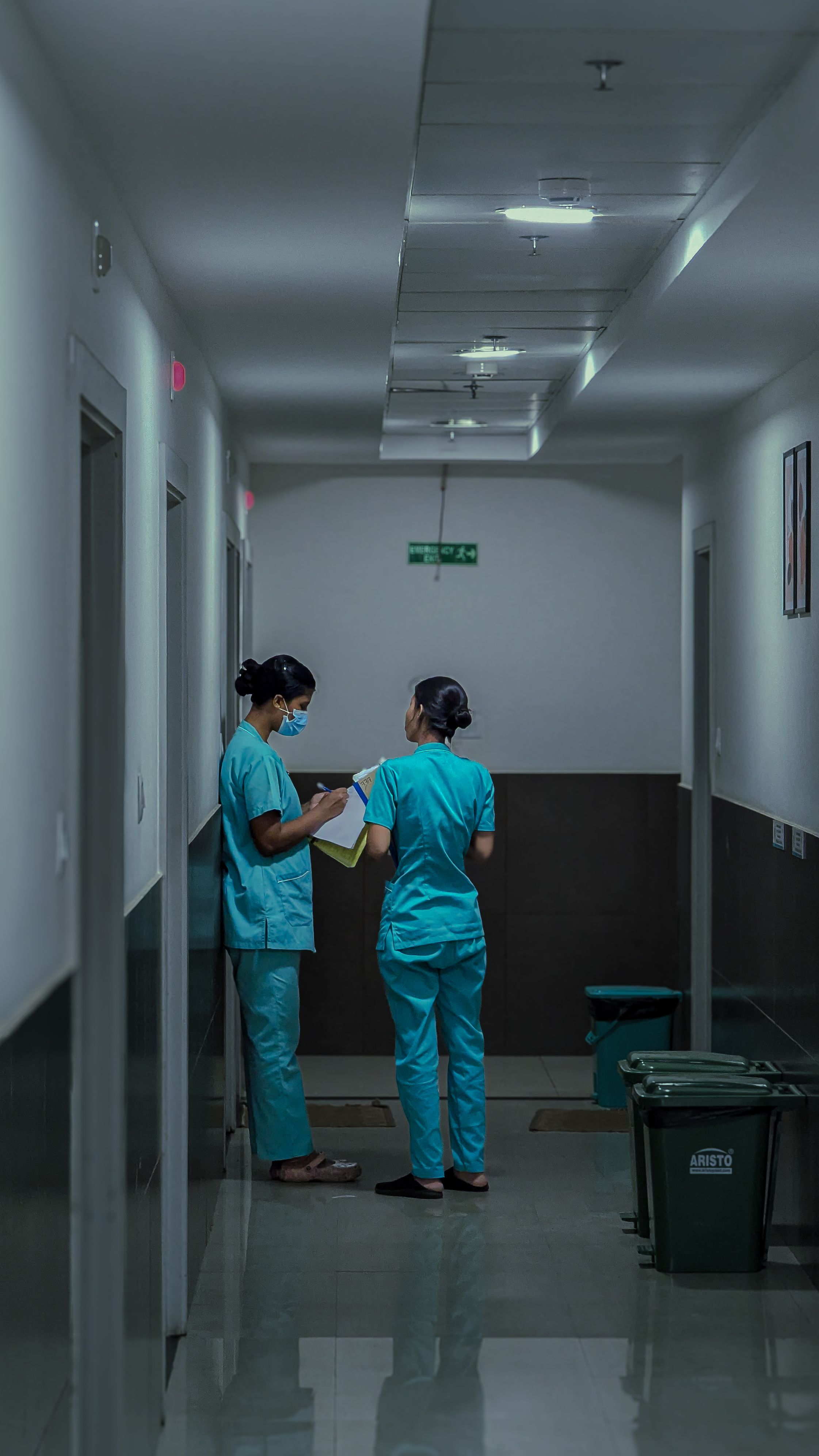 Two nurses in scrubs reviewing patient notes together in a hospital corridor