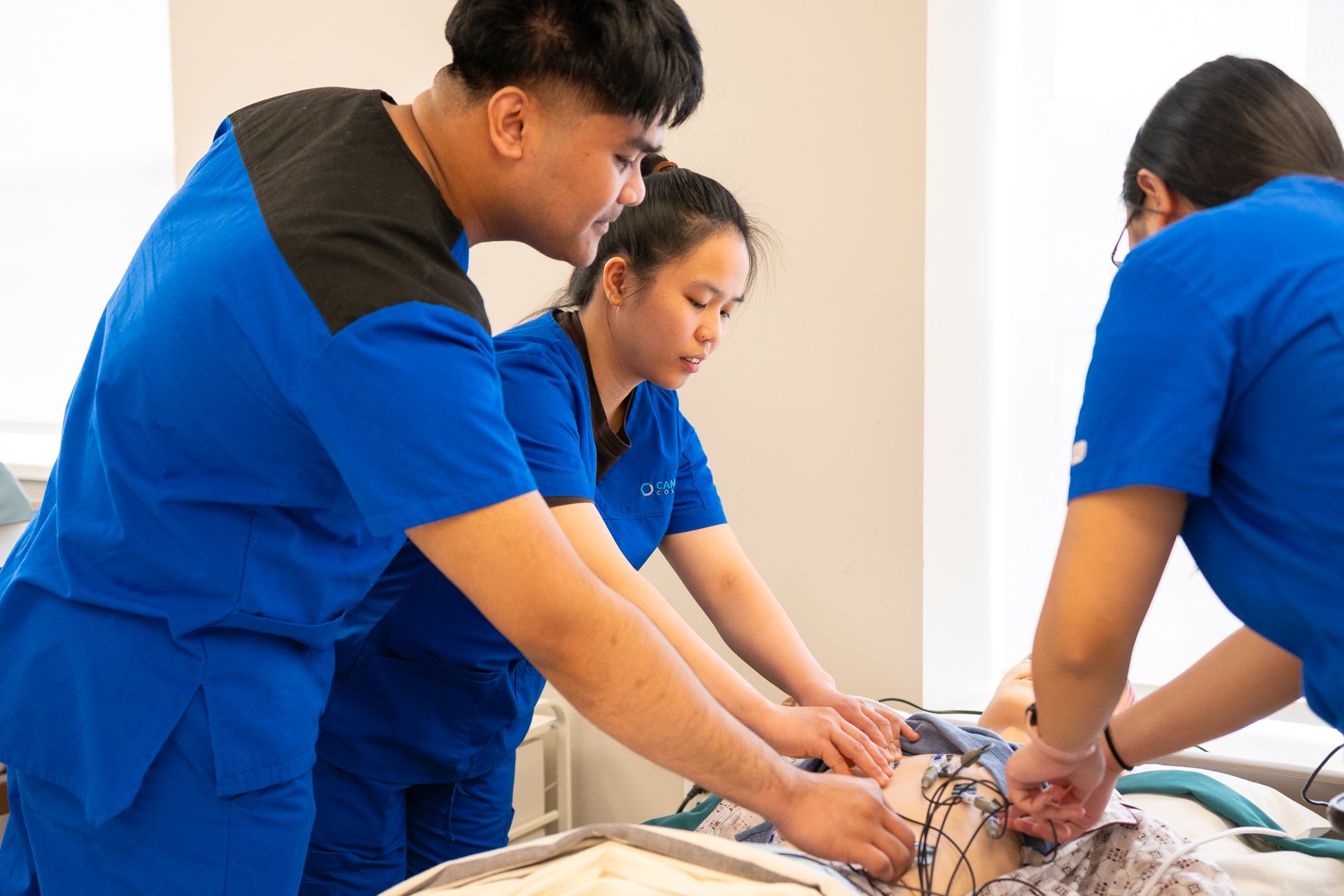 Nursing students in scrubs practising a clinical procedure together in a training room