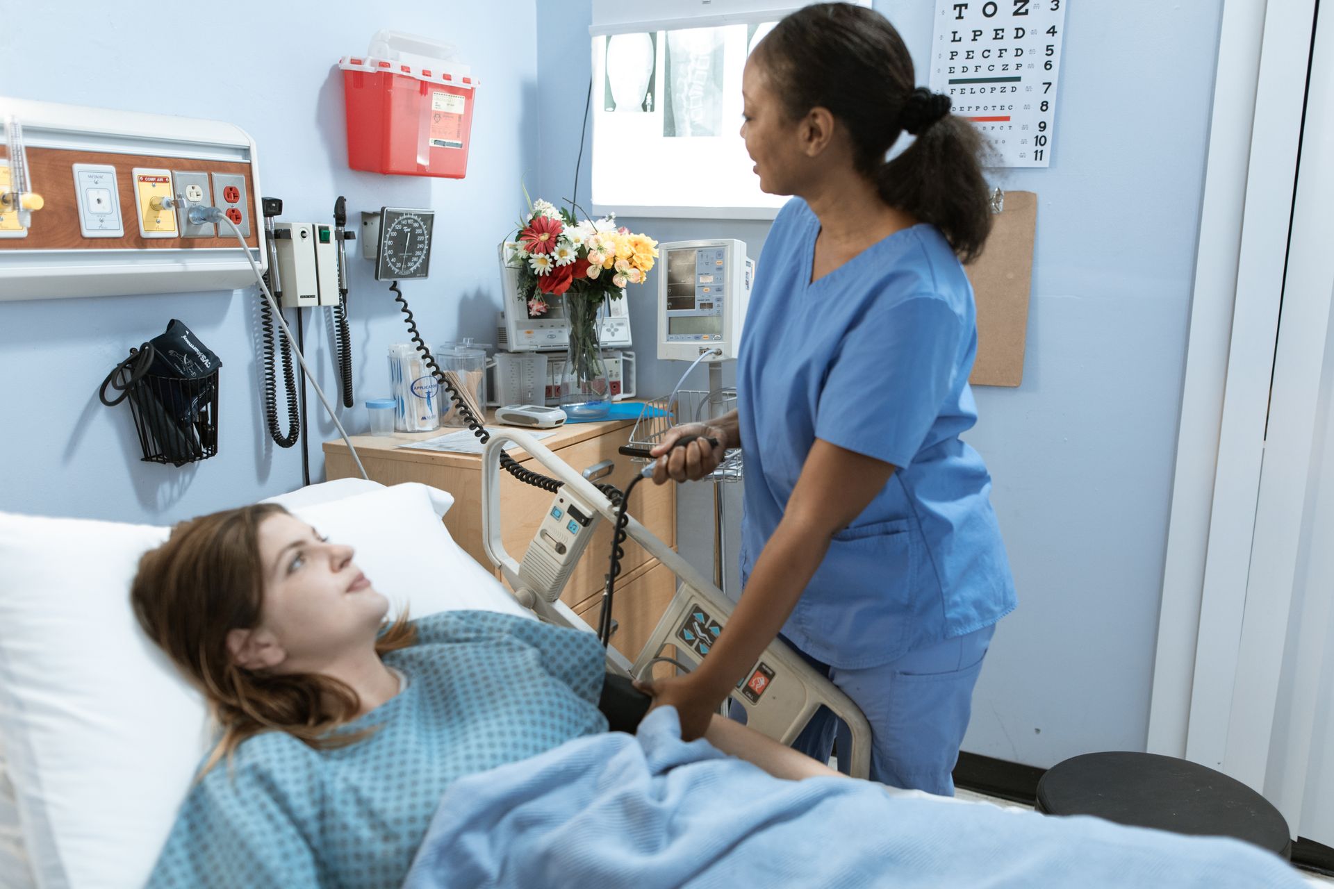 A nurse attending to a patient in a hospital room beside monitoring equipment