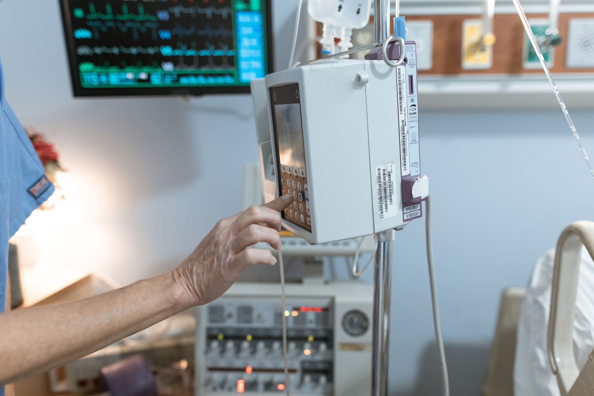 A hand setting up an infusion pump beside a patient monitor